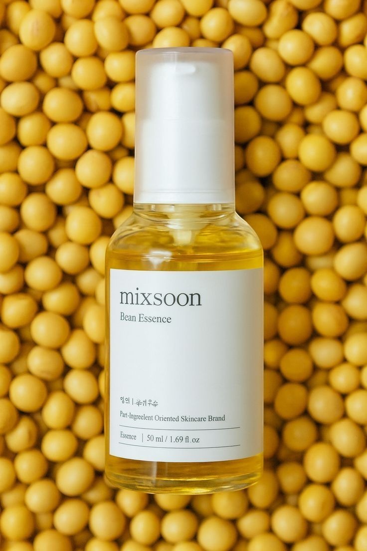 Saerún Skin: Botella de esencia Mixsoon Bean Essence con textura líquida dorada, sobre un fondo de frijoles de soja amarillos.
